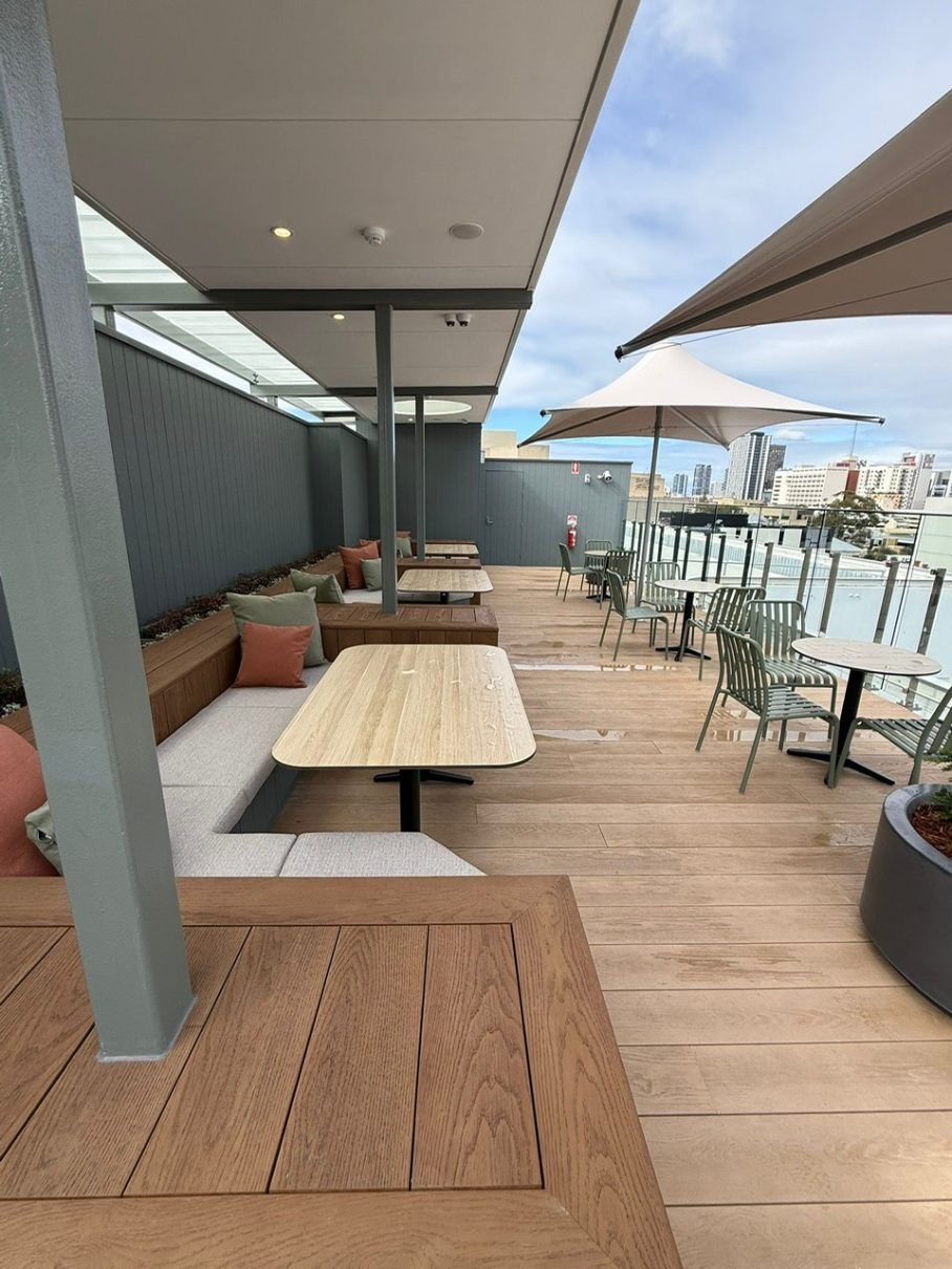 Outdoor restaurant patio with wooden tables, gray walls, and white umbrellas overlooking a waterfront view