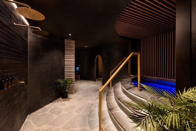 Curved indoor walkway with stone floor, wooden handrail, dark walls, and blue accent lighting