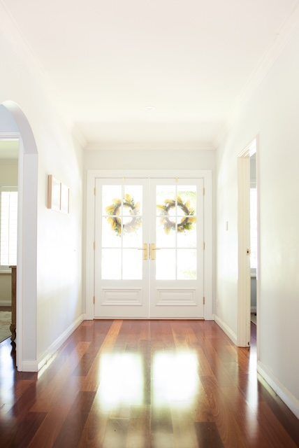 Bright hallway with polished wooden floors leading to white double doors with wreaths.