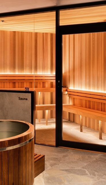 Warm wooden sauna interior with glass door and benches behind a stone floor.