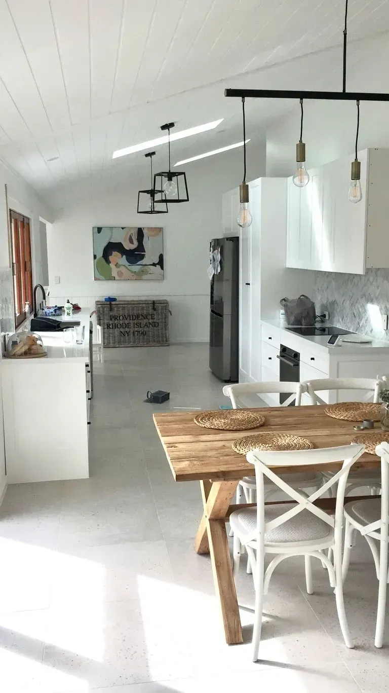 Bright modern kitchen-dining area with white cabinets, wood table, and hanging pendant lights