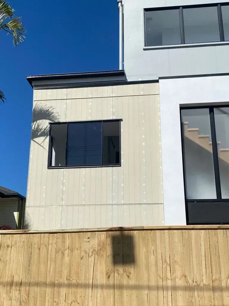 Modern house exterior with white walls, black-trimmed windows, and a wooden fence under a blue sky