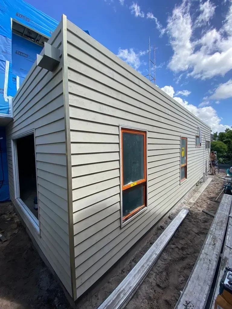 New beige siding on a narrow house exterior with a small window and unfinished ground around it