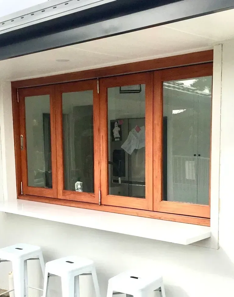 Wood-framed window on a white exterior wall above three white stools