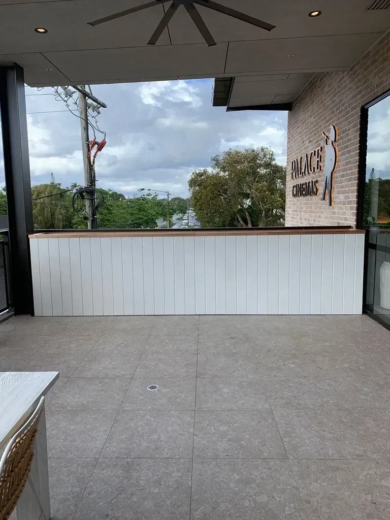 Outdoor patio with gray tile floor, white counter, brick wall, and cloudy sky beyond the opening