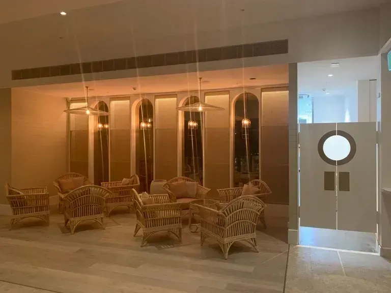 Wicker chairs arranged in a warm-lit lobby with mirrored walls and a glass door.