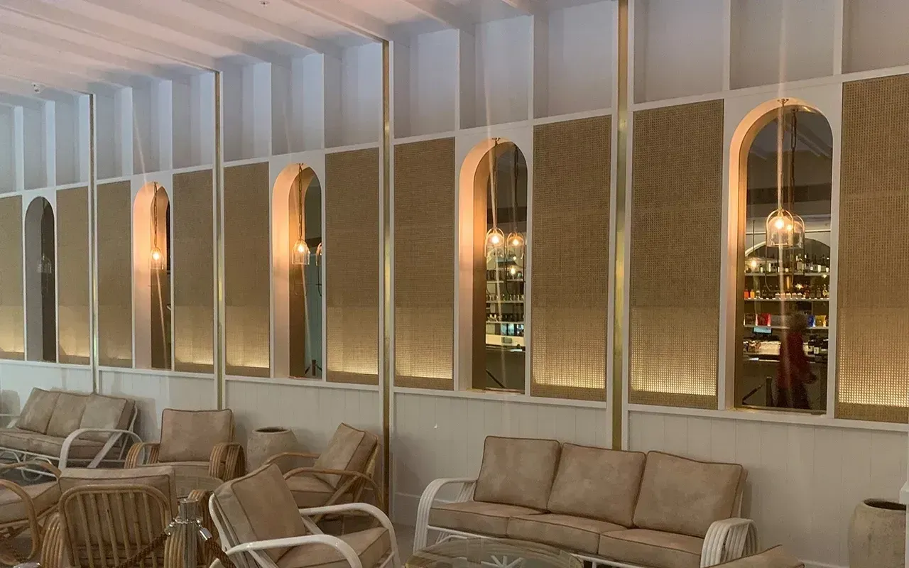 Cozy lounge with woven chairs and beige sofas along a wall of arched mirrors and warm pendant lights.
