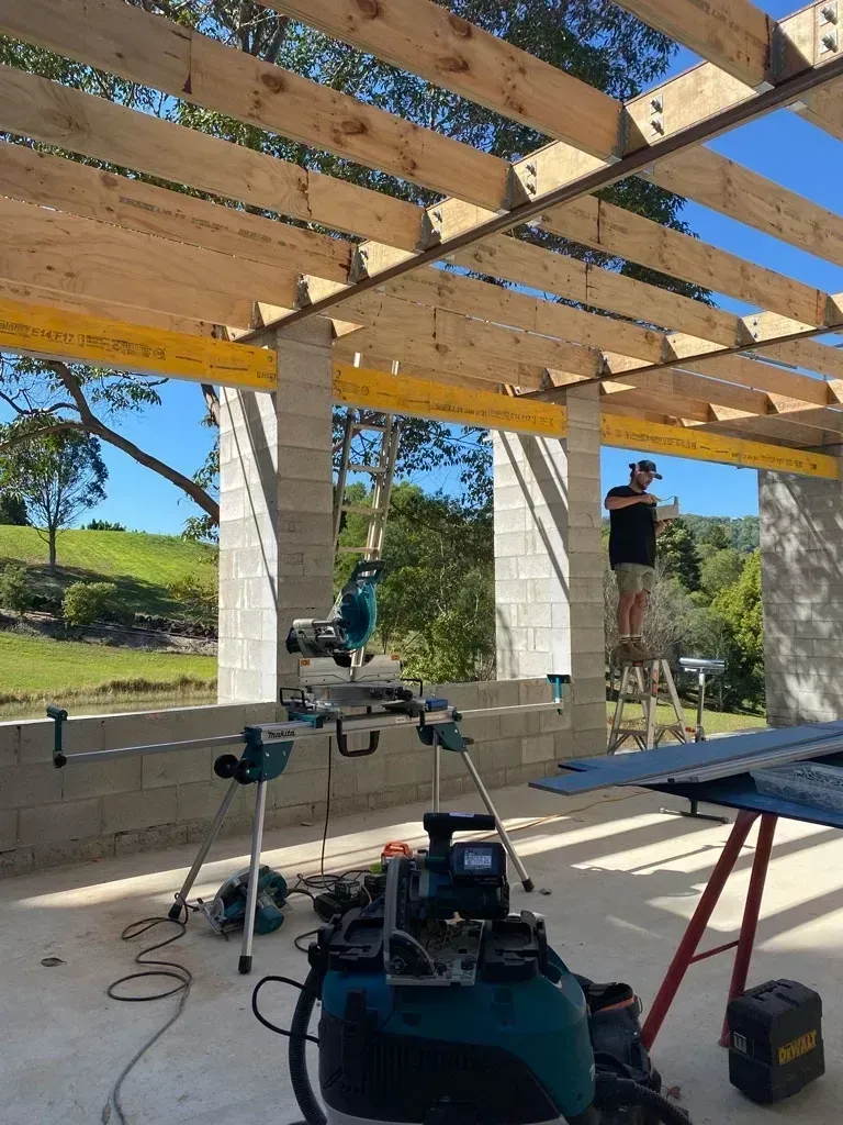 Two workers installing roof beams in a sunlit timber-framed house under construction