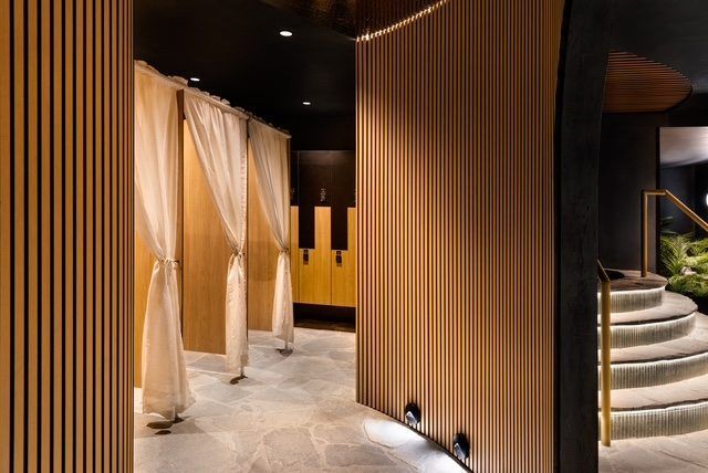 Elegant spa corridor with beige drapes, wood slat walls, and a curved staircase under soft lighting
