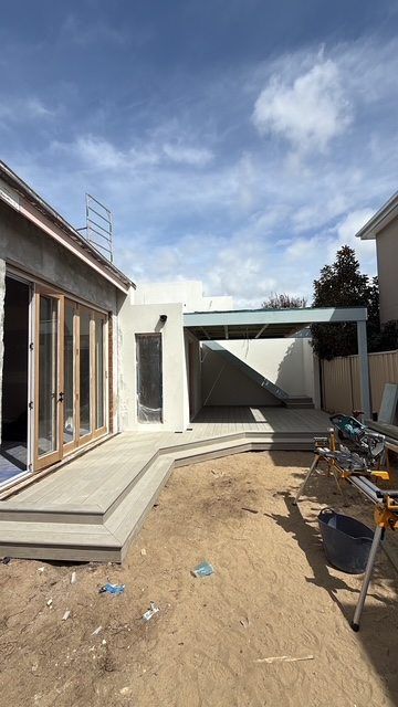Unfinished backyard patio with construction materials, concrete steps, and a covered pergola frame.