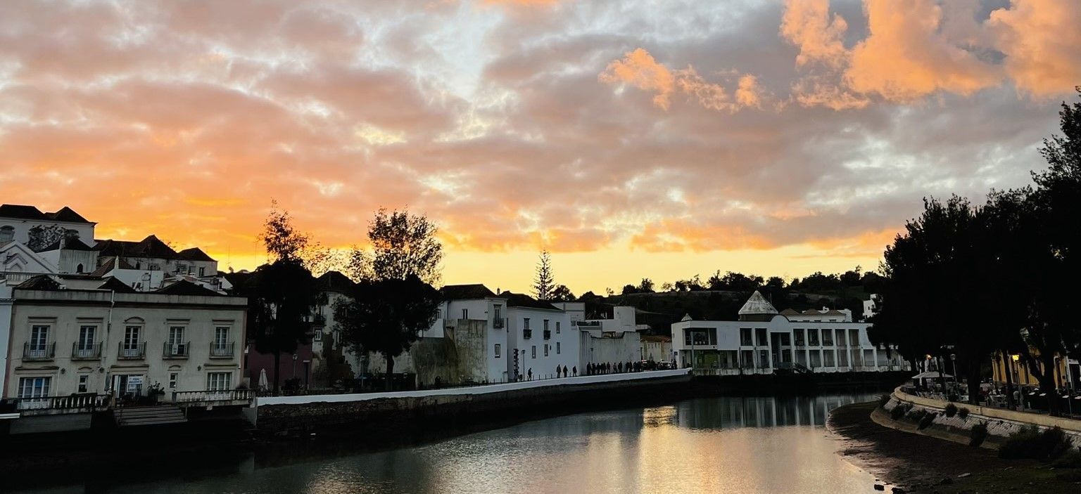 Zonsondergang boven een kalme rivier met witte gebouwen langs de oevers.