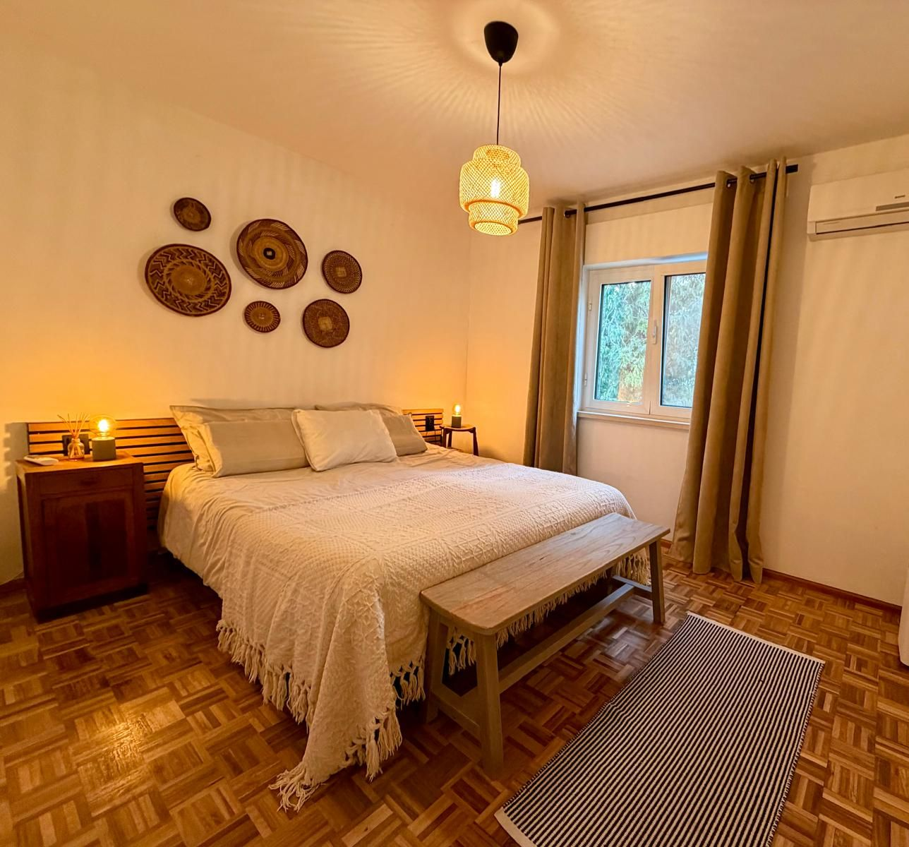 Slaapkamer met wit beddengoed, geweven wanddecoratie en een papieren kroonluchter; warme verlichting.