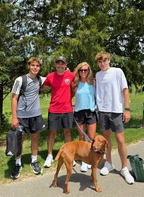 Four people and a brown dog posing outdoors in front of trees.