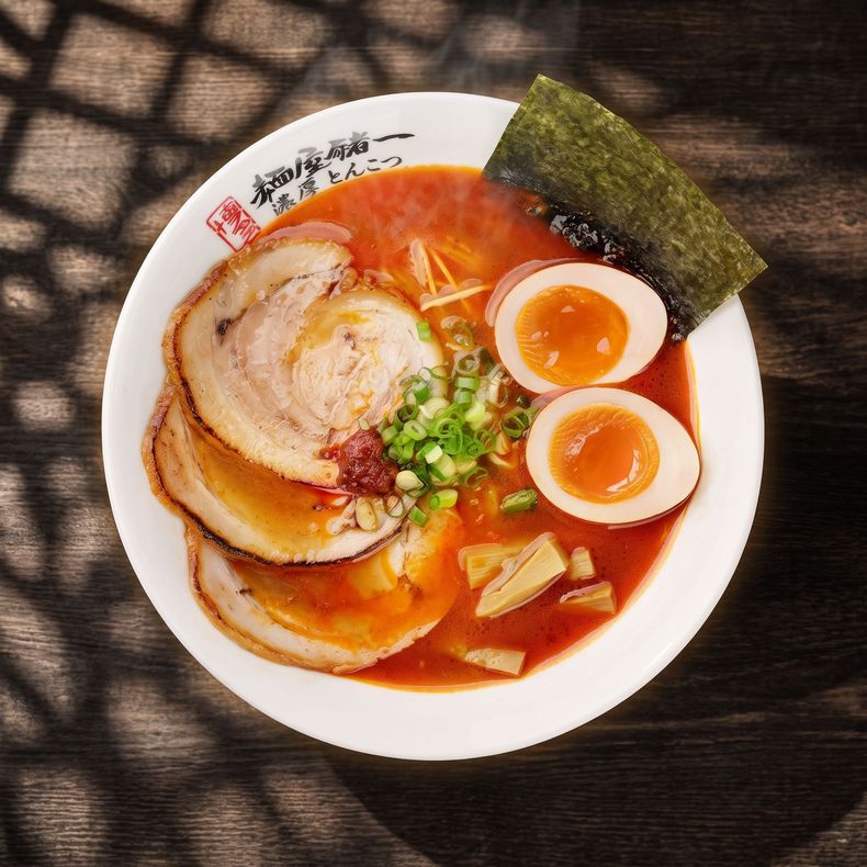 Ramen bowl with sliced pork, soft-boiled eggs, nori, and green onions in rich red broth