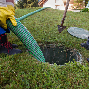 Worker using green hose to clean out a yard drain hole beside a shovel and grass