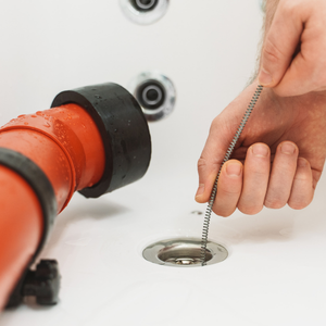 Hand opening a sink drain with a red pipe wrench nearby