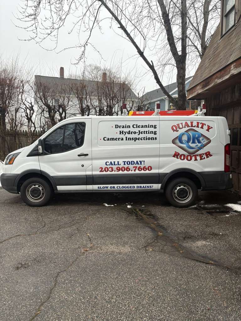 White plumbing service van parked on a wet street with “Quality” logo and company text.