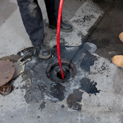 Worker using a red cable to clear a clogged drain in a wet concrete floor