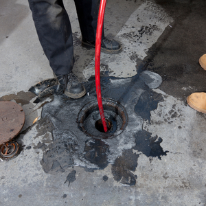 Worker using a red cable to clear a clogged drain in a wet concrete floor