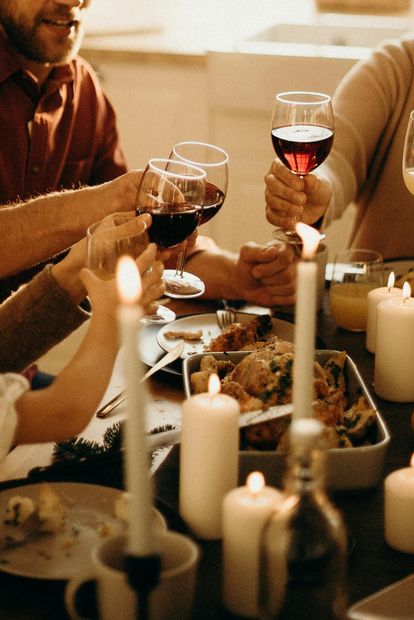 A group of people are sitting at a table toasting with wine glasses to celebrate a good meal together.