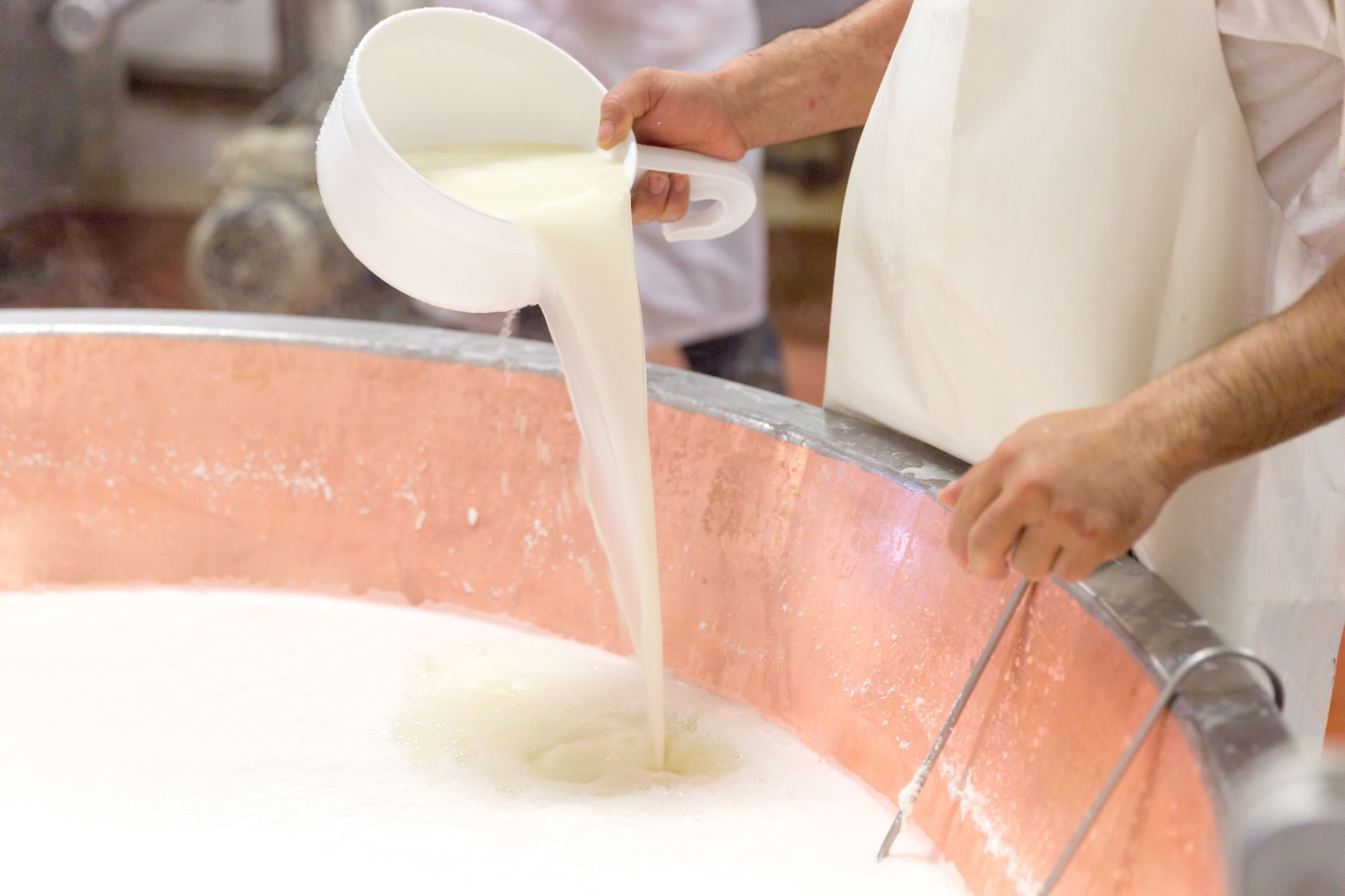 A person is pouring milk into a large copper pot.