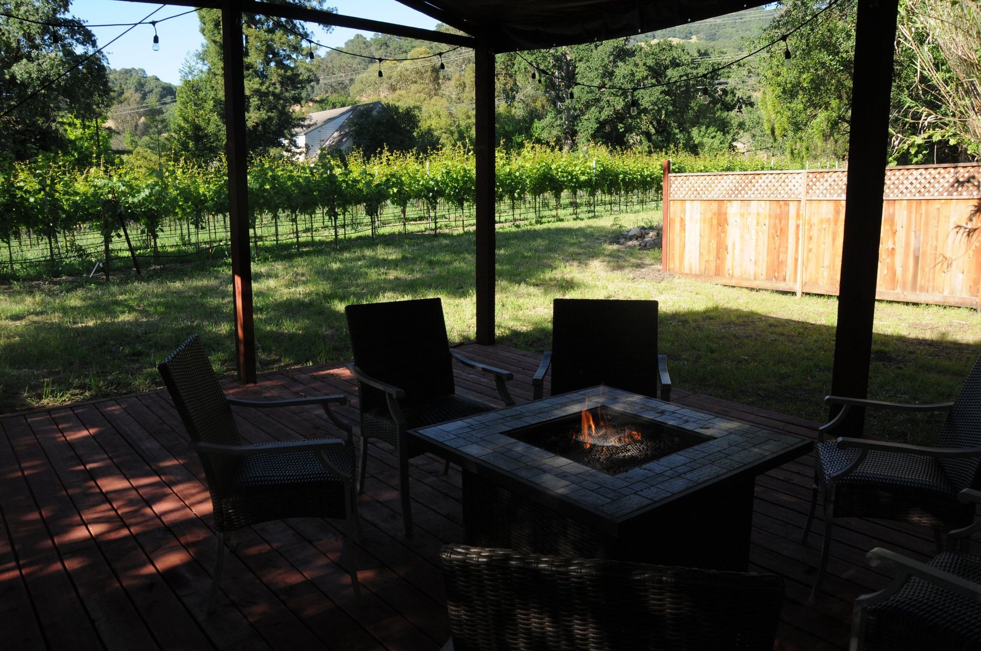A patio with a fire pit and chairs with a vineyard in the background