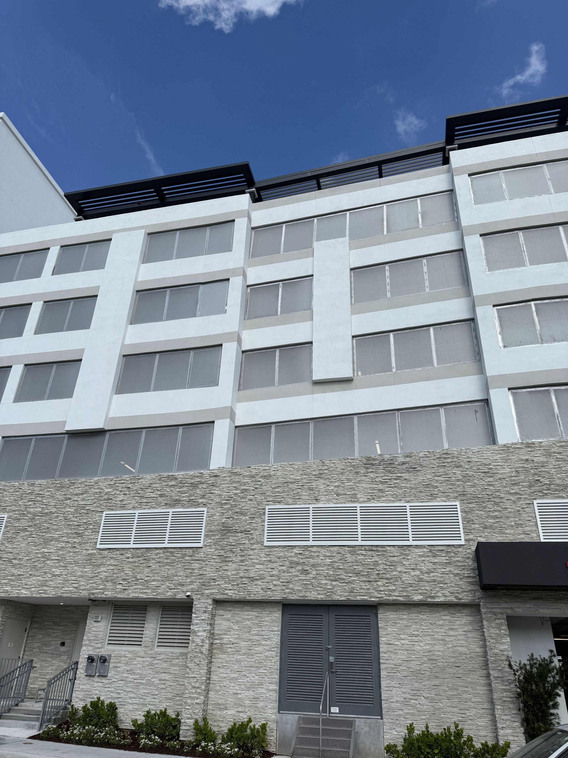 Modern white building with stone base and mirrored windows against a blue sky.