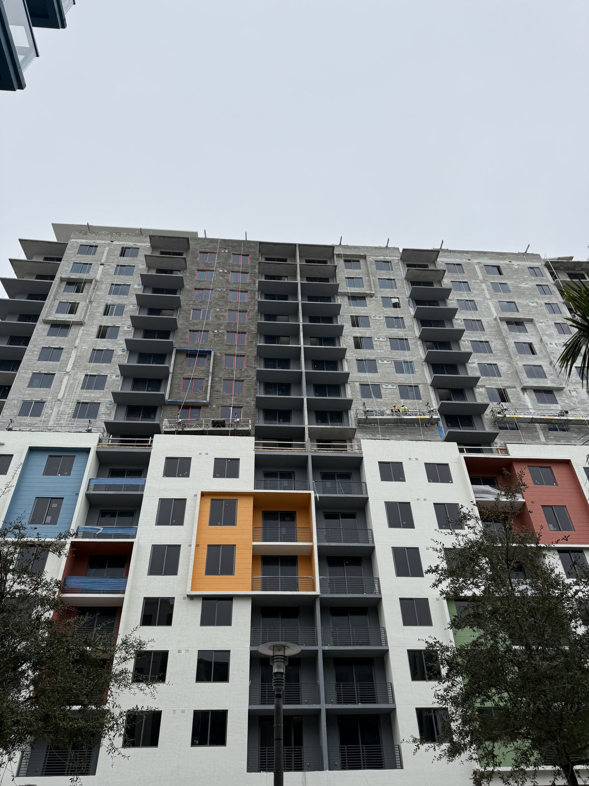 Multistory building under construction; white facade with colorful accent panels and balconies.