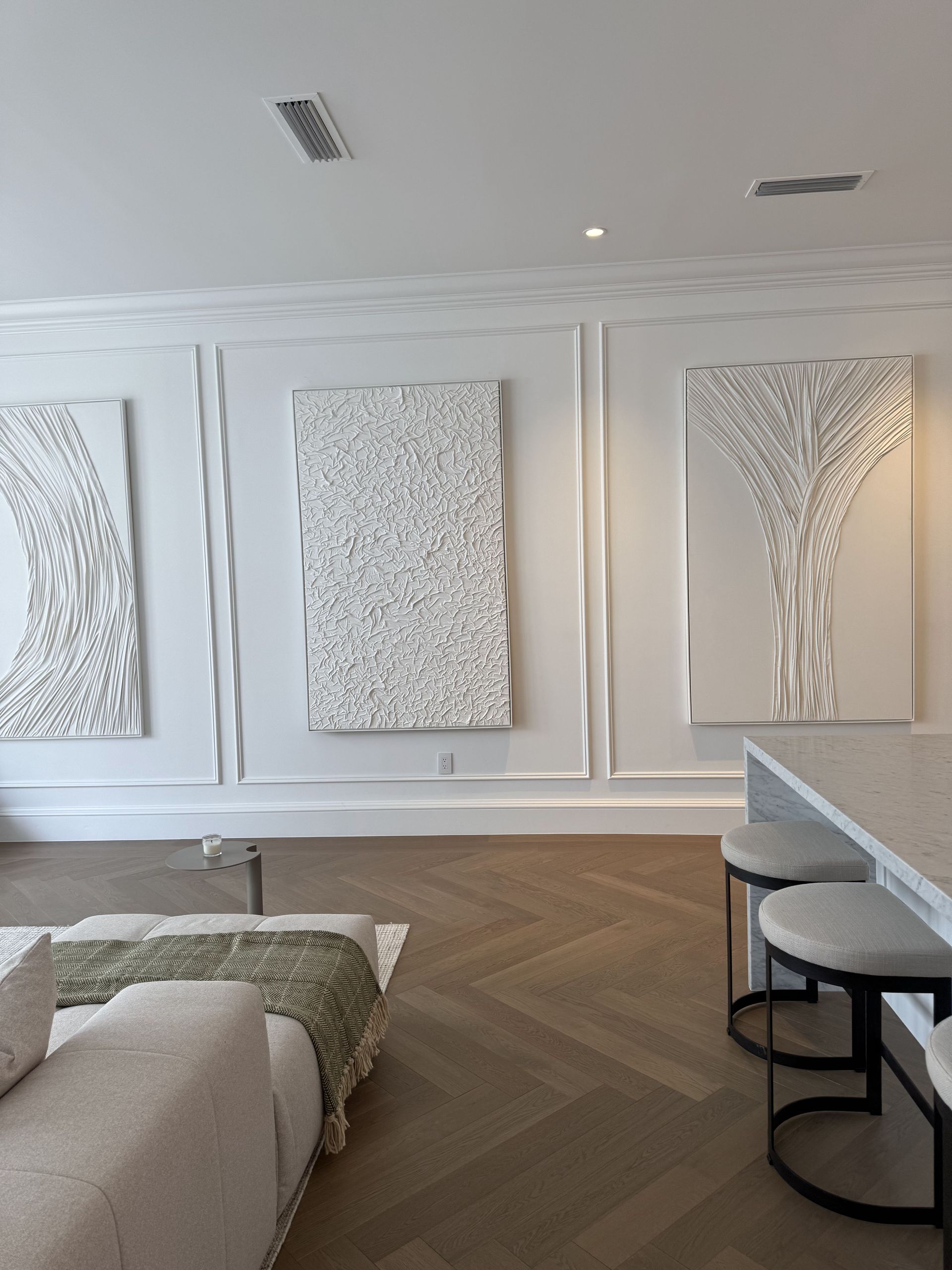 White modern art on a wall, with a sofa and stools. Wooden floor.