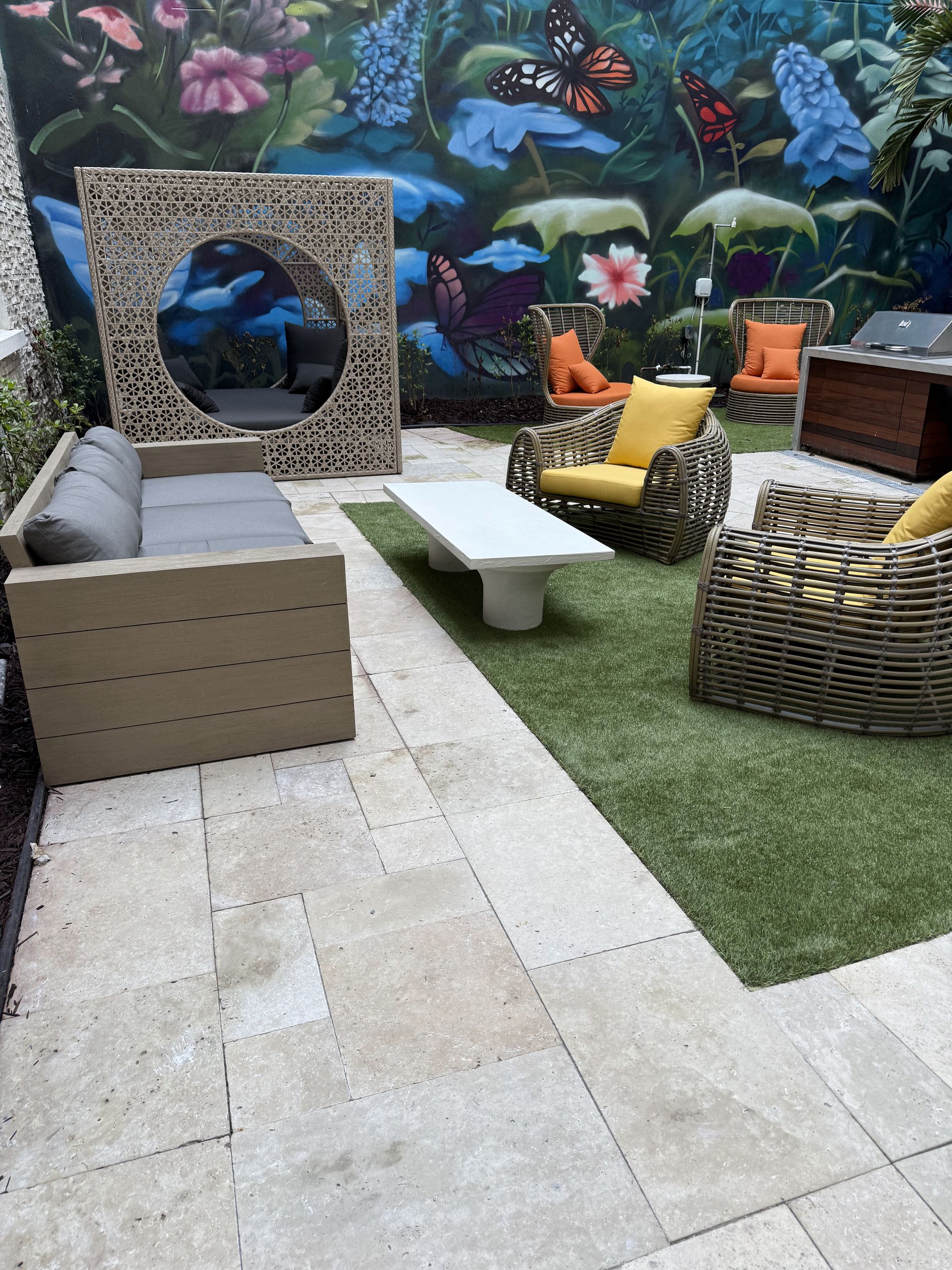 Outdoor patio with wicker furniture, a white table, and a mural of flowers and butterflies.