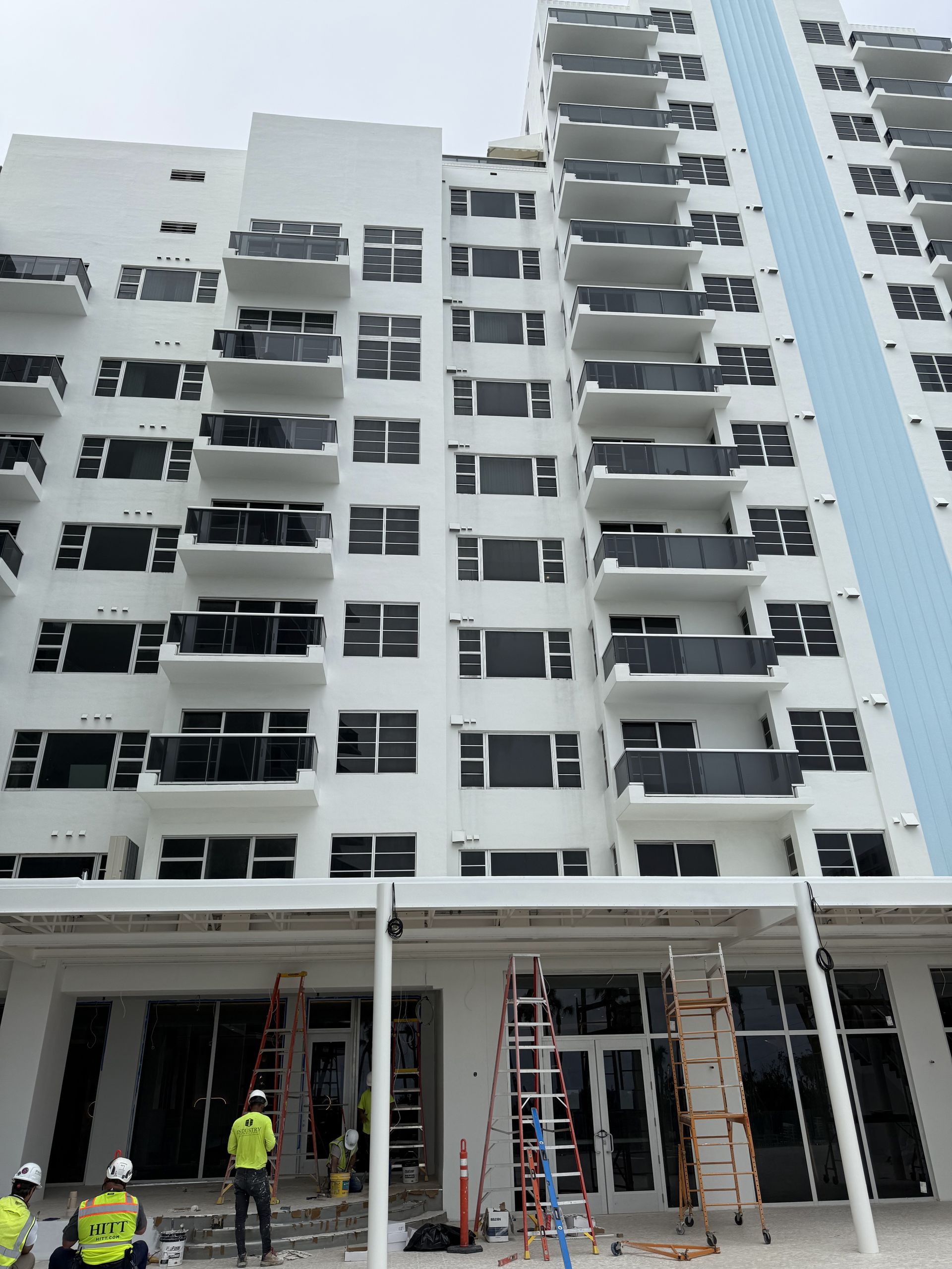 Exterior of tall white building under construction, workers at the base, balconies.
