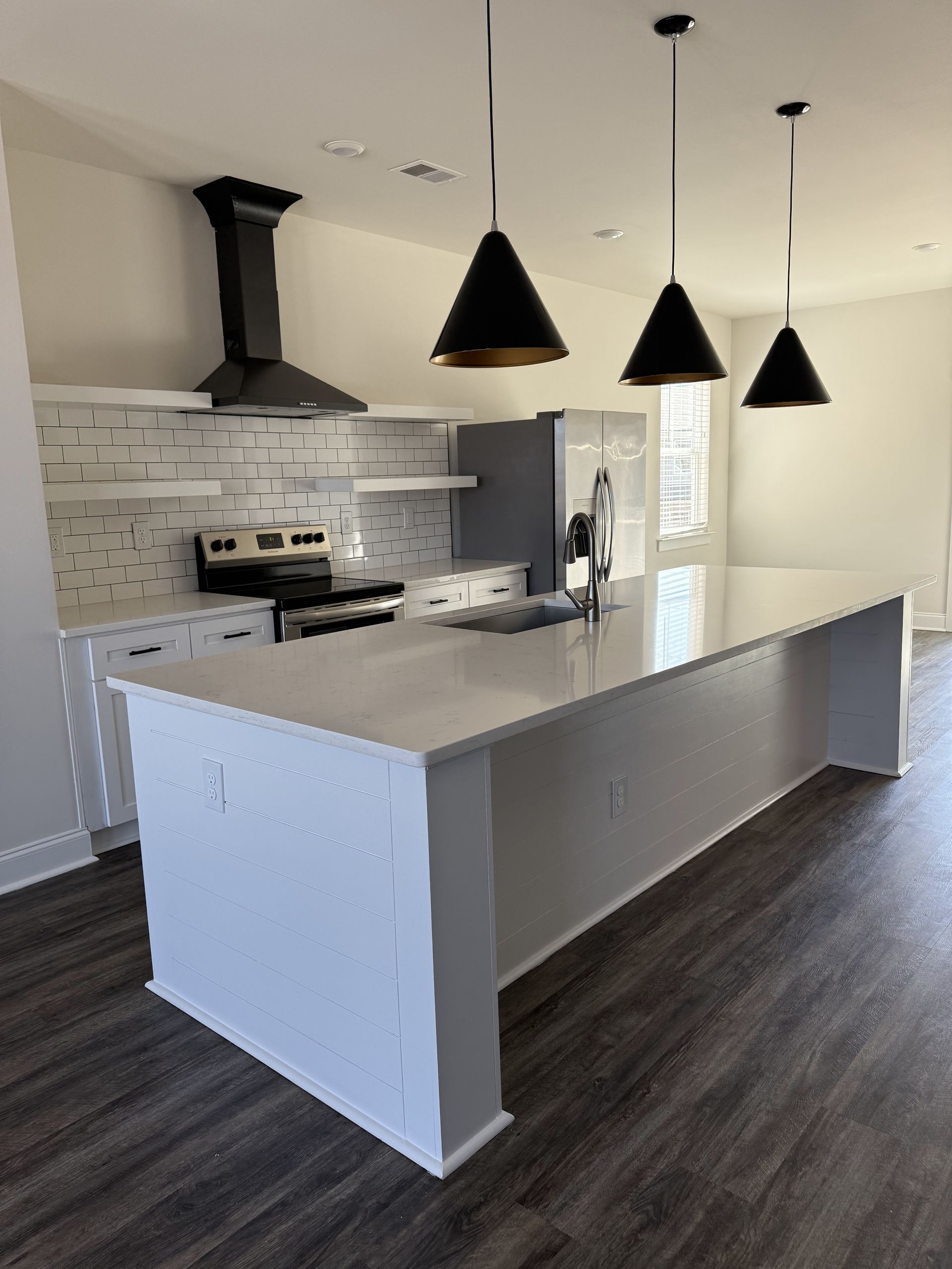 Modern kitchen with white countertops, black pendant lights, and stainless steel appliances. Dark wood flooring.