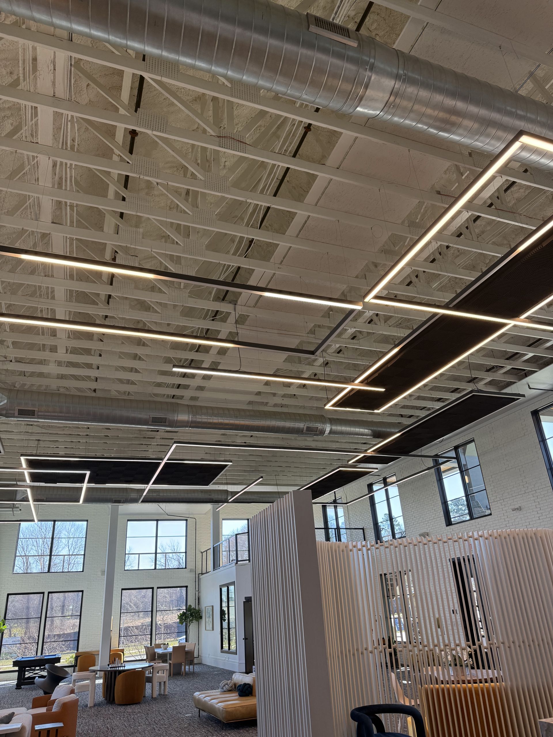 Interior shot with exposed concrete ceiling, recessed lighting, and large windows. Furnishings in foreground.