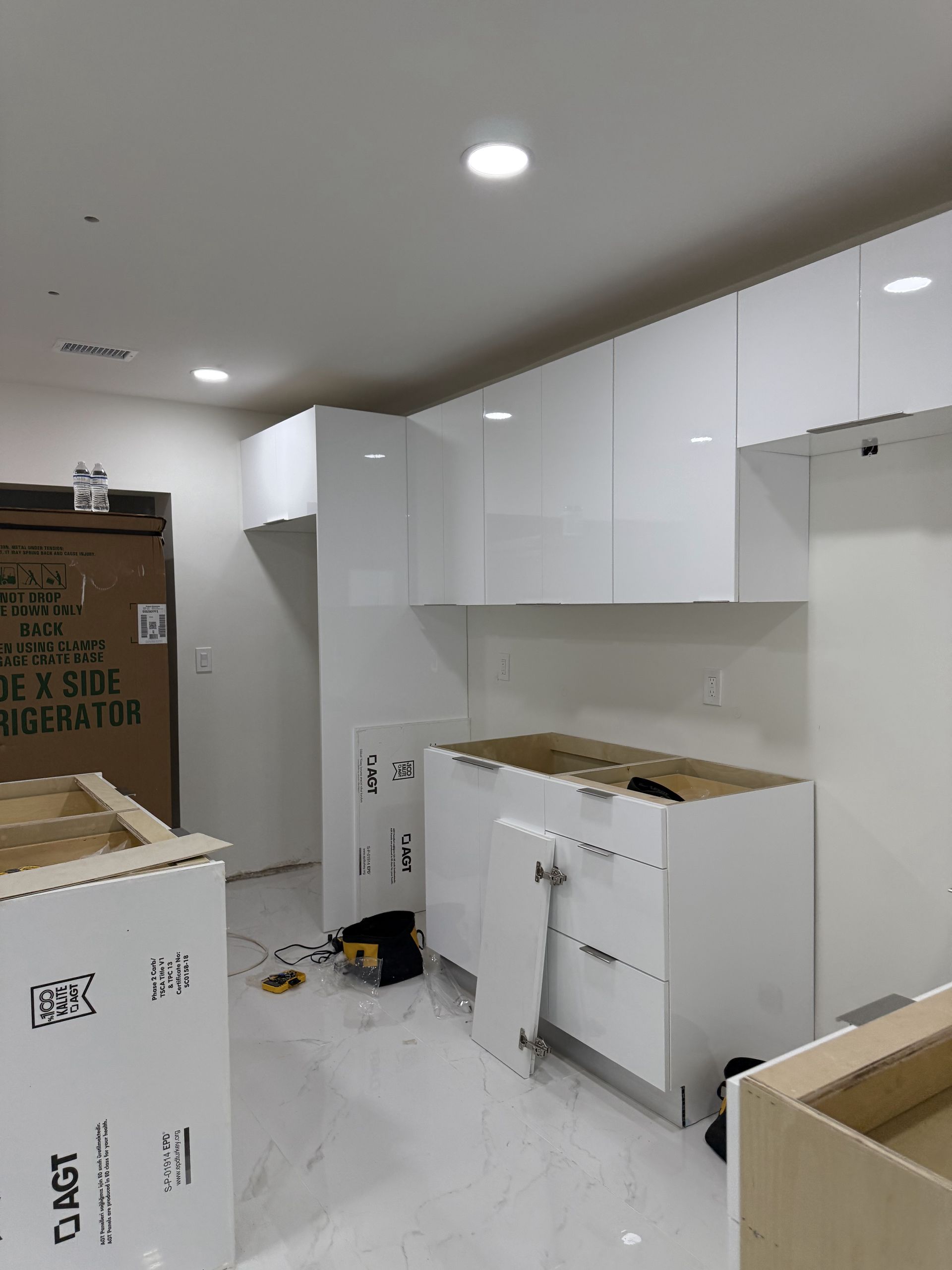 Modern white kitchen with cabinets being installed, unfinished countertop, and boxes.