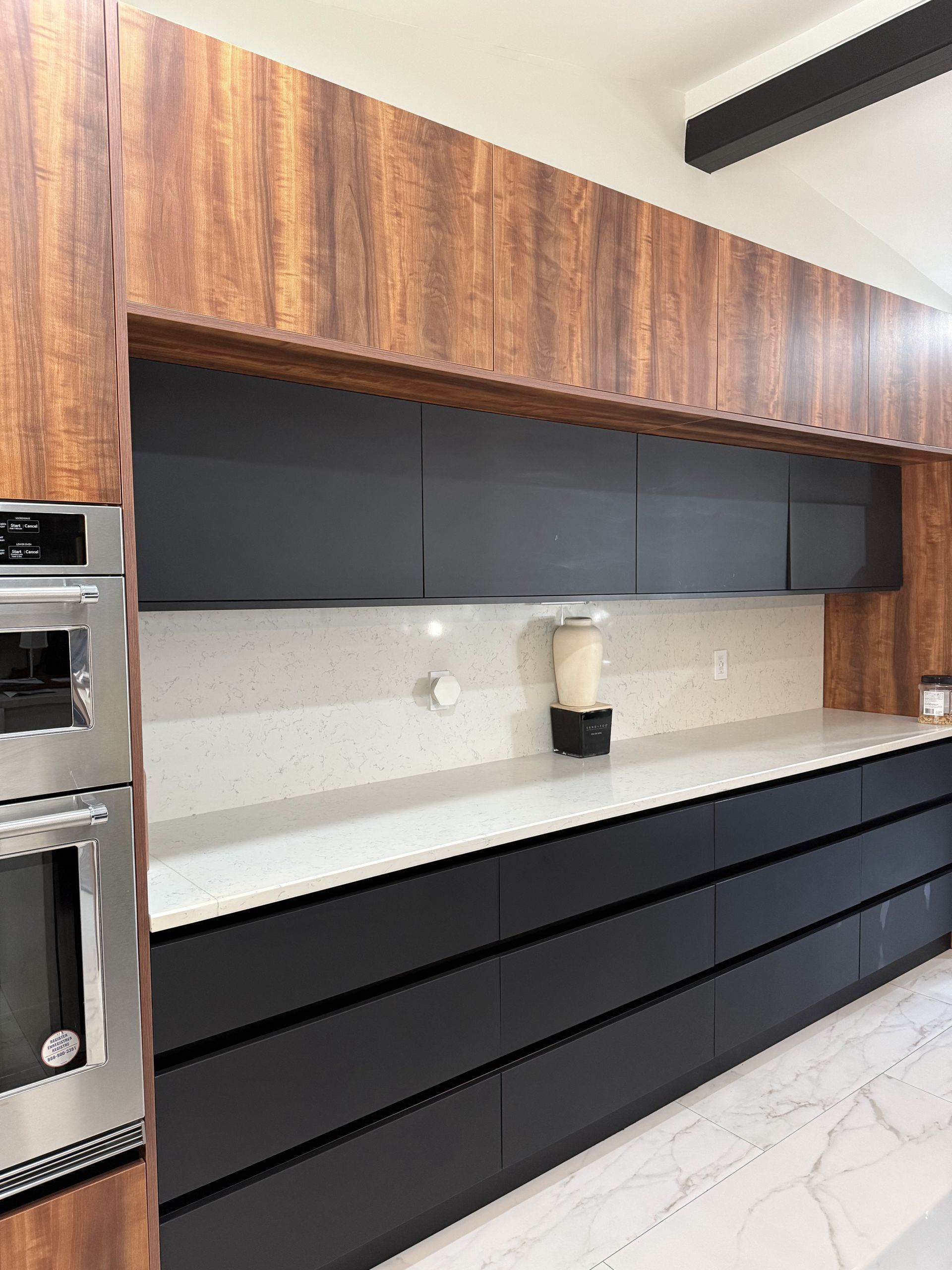 Modern kitchen with black and wood-tone cabinets, white countertop, and built-in oven.