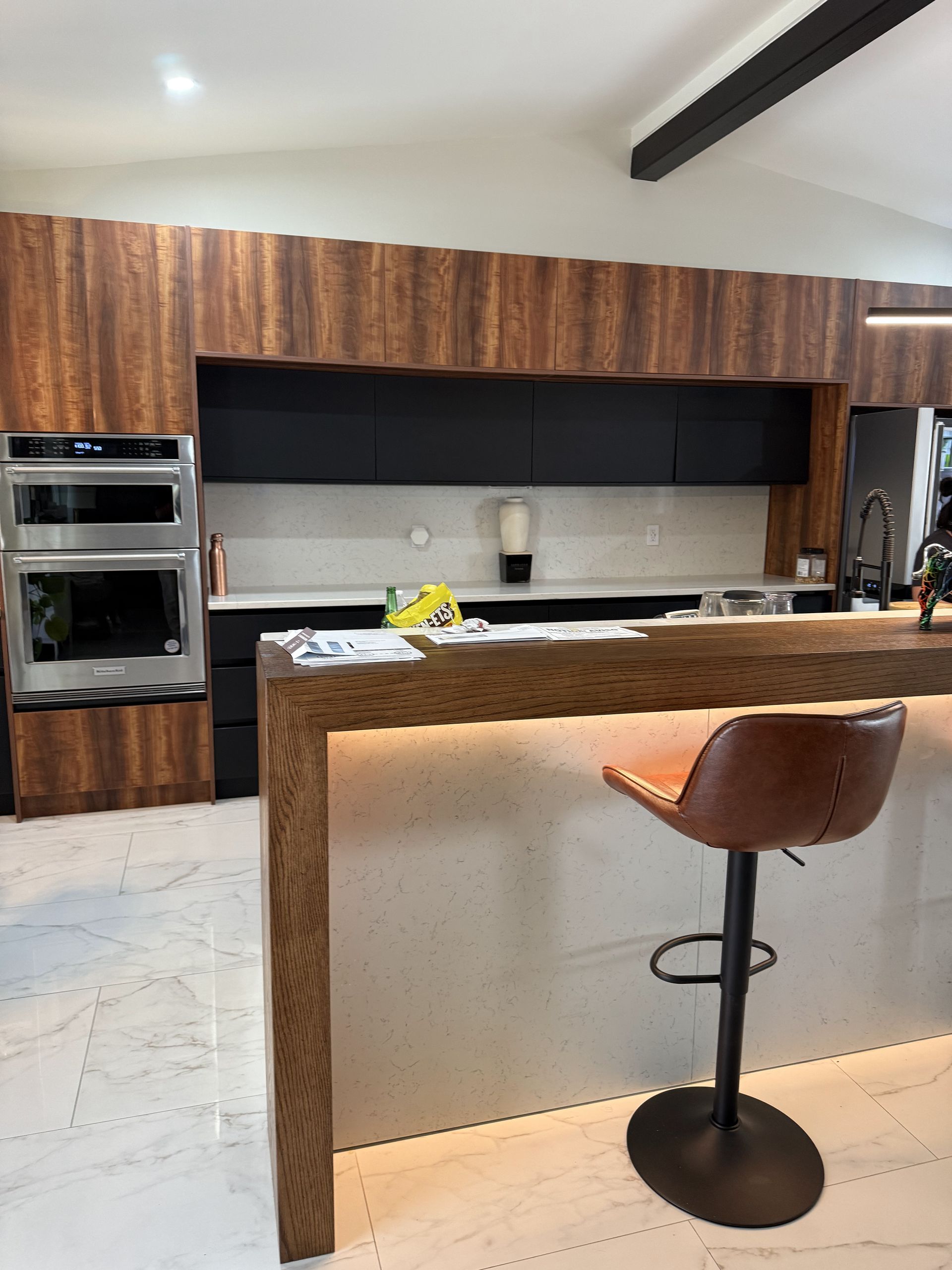 Modern kitchen with wood cabinetry, black accents, and a marble countertop. 