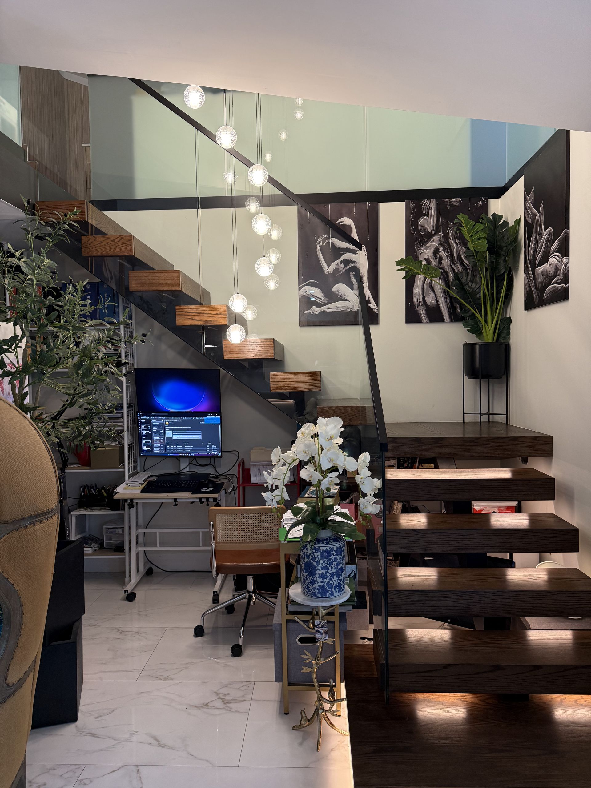 Open staircase with wooden treads, desk with computer, and hanging lights.