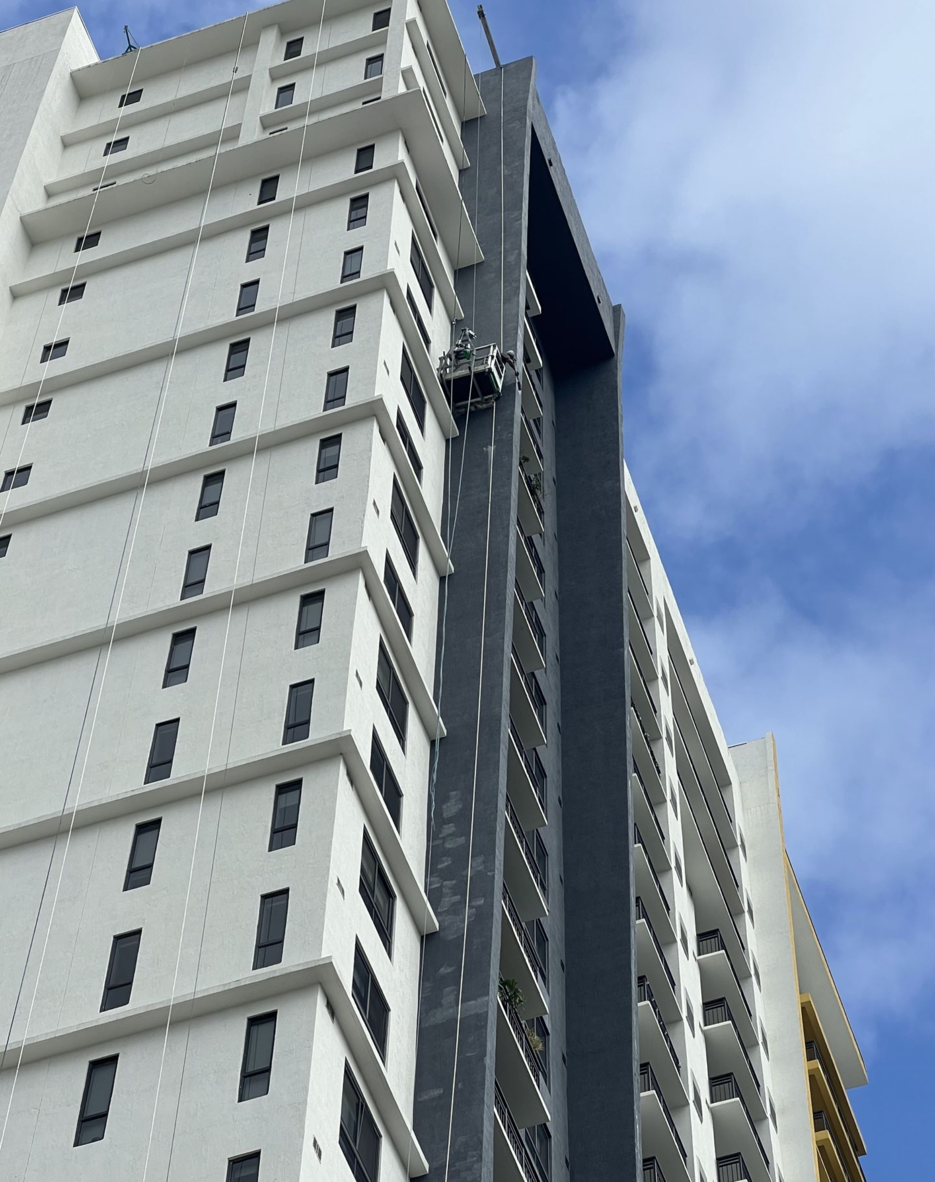 High-rise building with a maintenance lift. White and gray facade with a blue sky in the background.