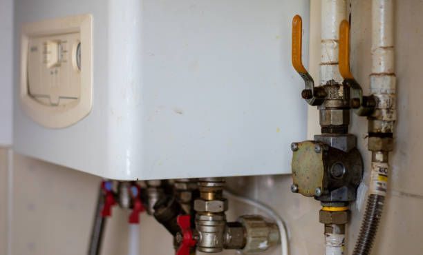 Close-up of a white wall-mounted boiler with pipes and valves underneath