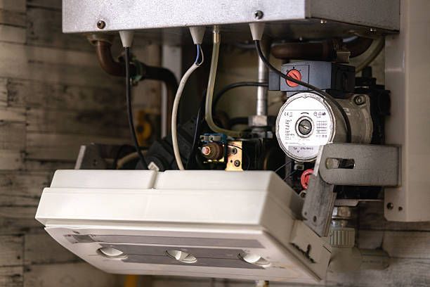 Close-up of an indoor boiler or HVAC unit with pipes, wiring, and a control gauge.