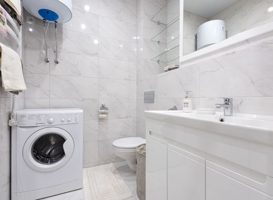 Small white bathroom with a washing machine, toilet, sink, and wall-mounted water heater
