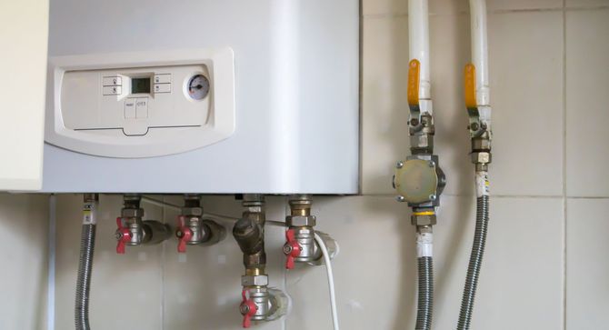 Wall-mounted boiler with exposed pipes and two yellow-handled shutoff valves below it.