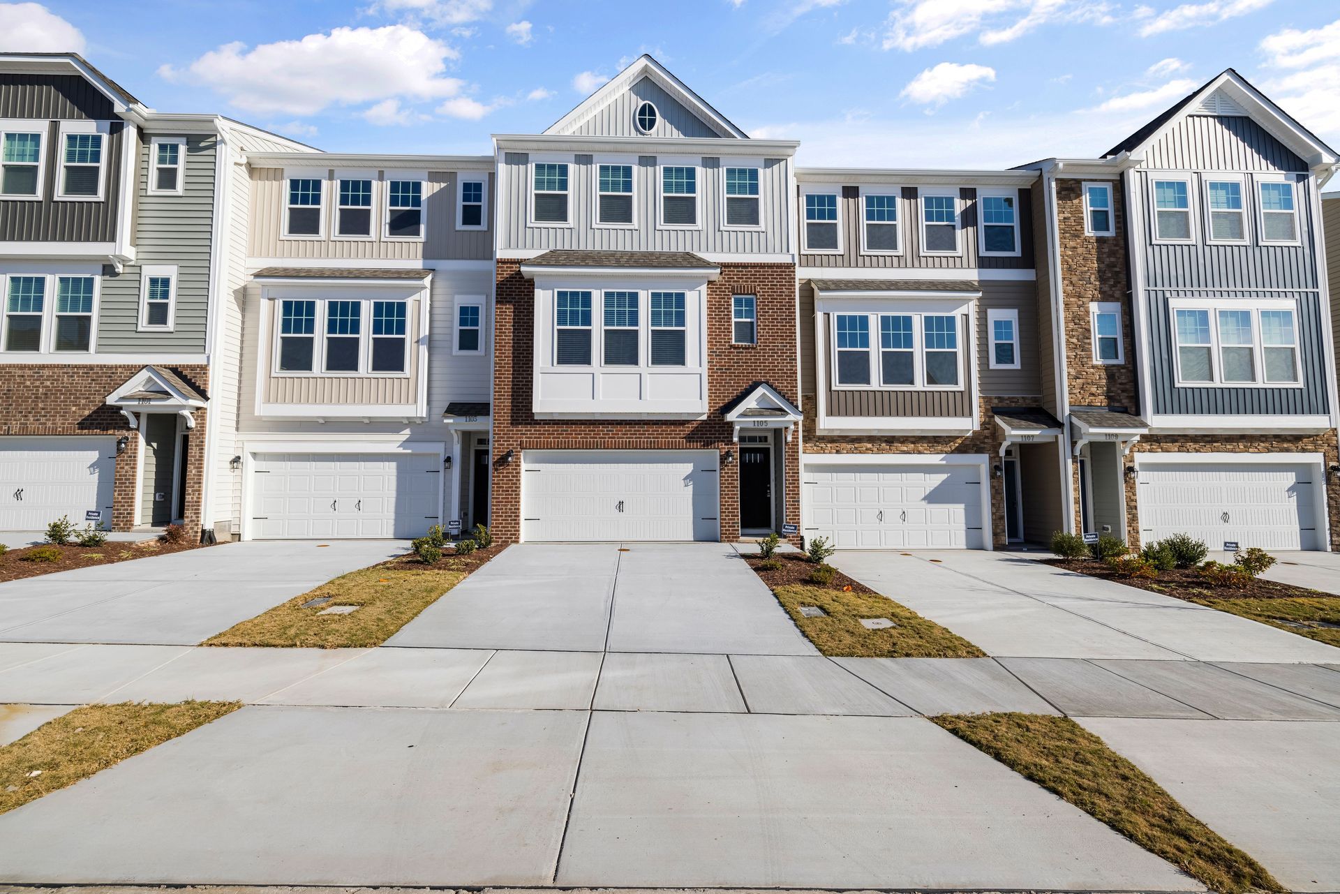 Row of modern gray townhouses with garages and driveways under a blue sky