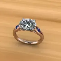 Rose gold solitaire engagement ring with a large round diamond and blue accents on a wood surface