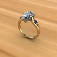 Gold ring with a large oval diamond and a small blue gemstone on a wooden surface