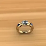 Gold ring with a square clear gemstone and blue side stones on a wooden surface