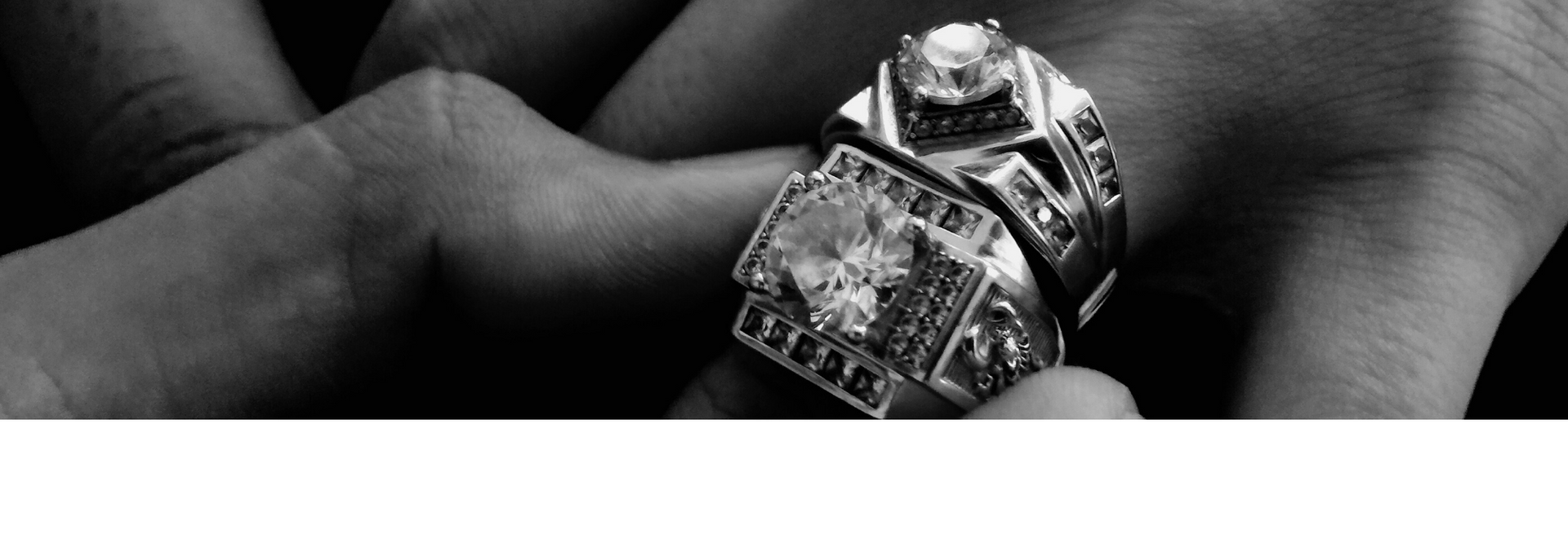 Hands holding a ring with a large square gemstone and ornate details in black and white.