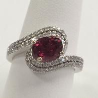 Silver swirl ring with a red gemstone on a white display stand