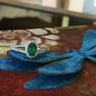 Green gemstone ring on a blue feathered fabric surface with a red patterned background