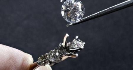 Jeweler holding a diamond ring with tweezers beside a mounted round diamond on a dark background